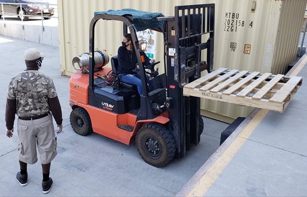 A woman operates a fork lift as a man watches