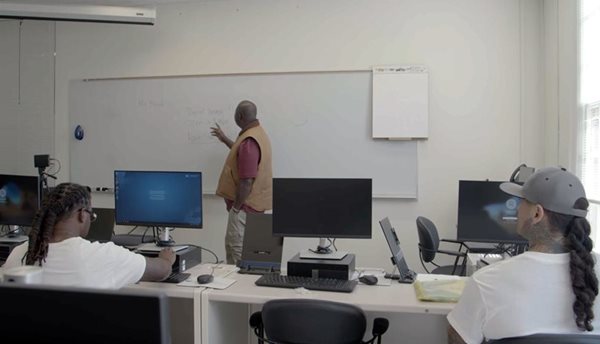 Students at computers listen to an instructor at a whiteboard