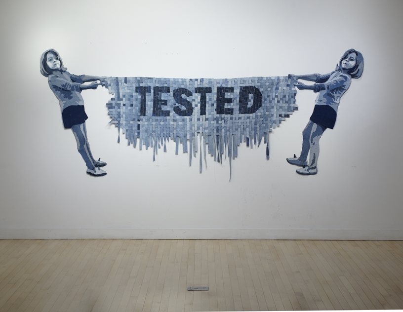 Two girls pulling on a piece of denim, which is melting, and has the word tested in big font and all caps