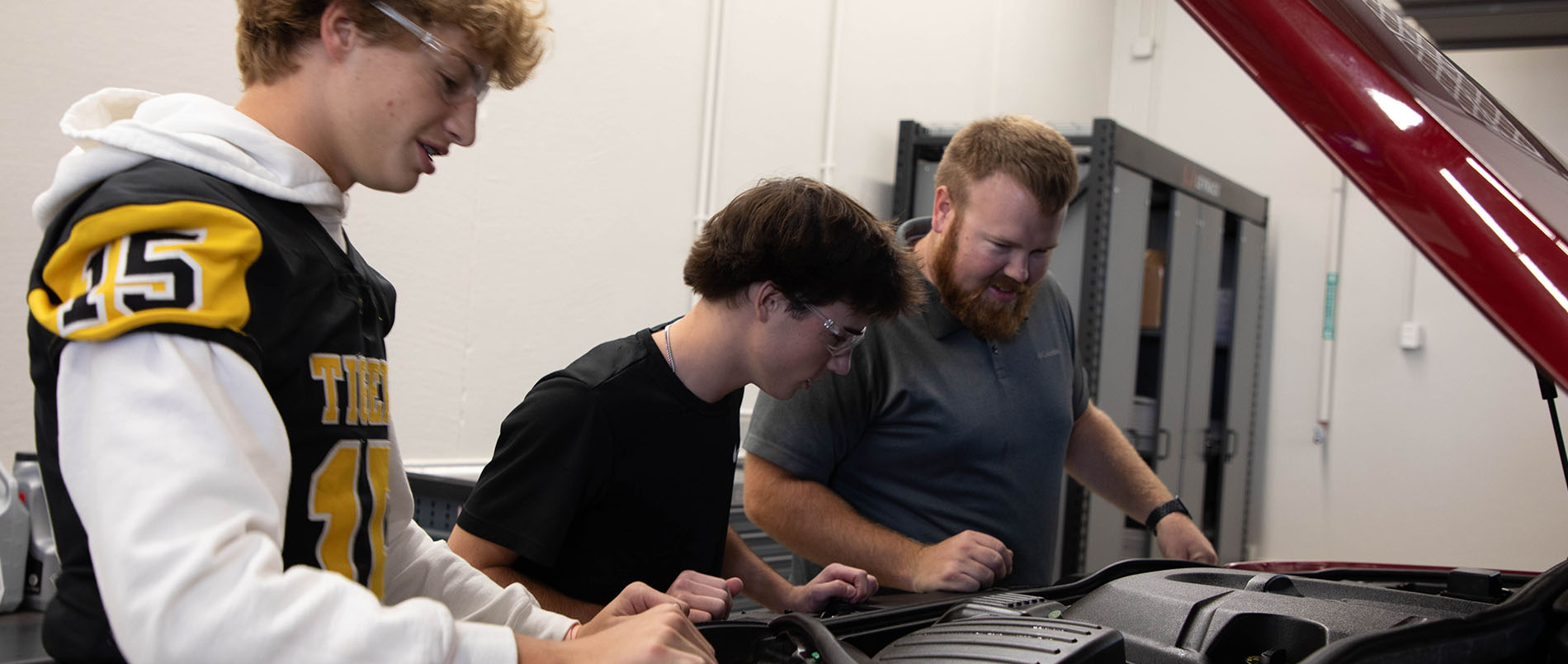 two automotive student working with an instructor under the hood of a vehicle