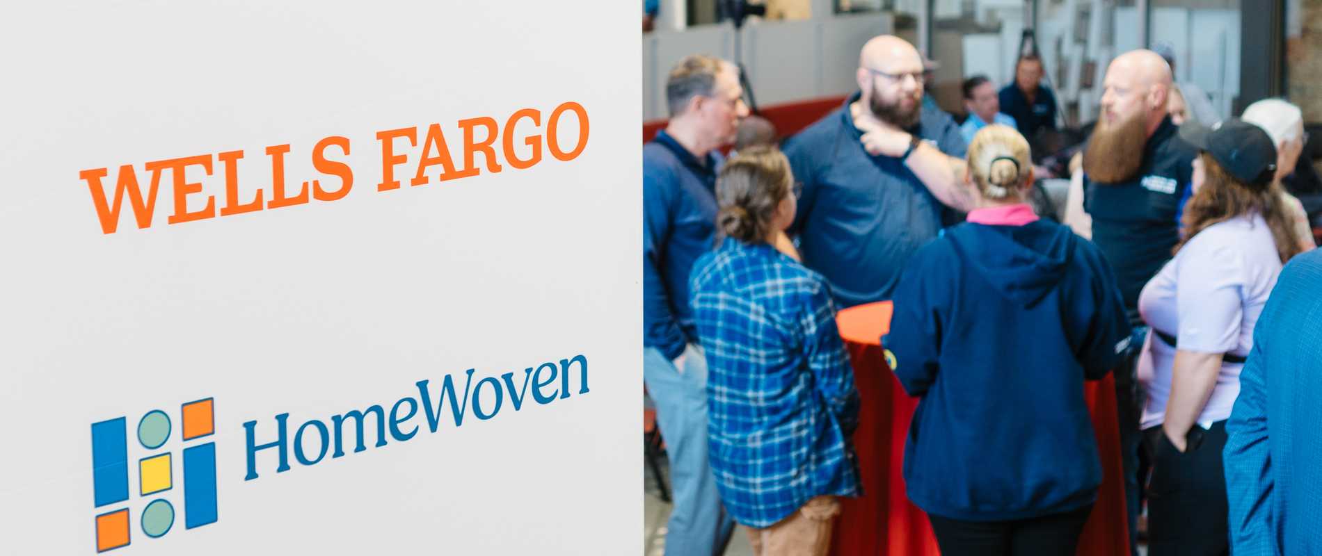 White sign with Wells Fargo and HomeWoven logos in focus with group of people in background