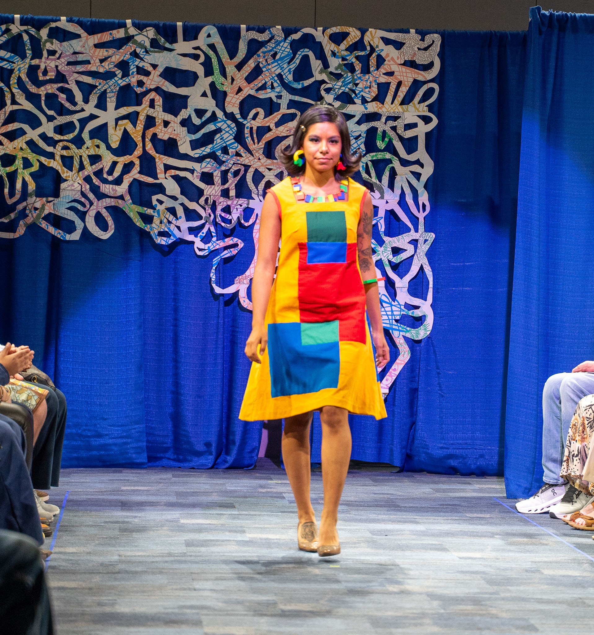 Student model in multi colored dress walking down runway