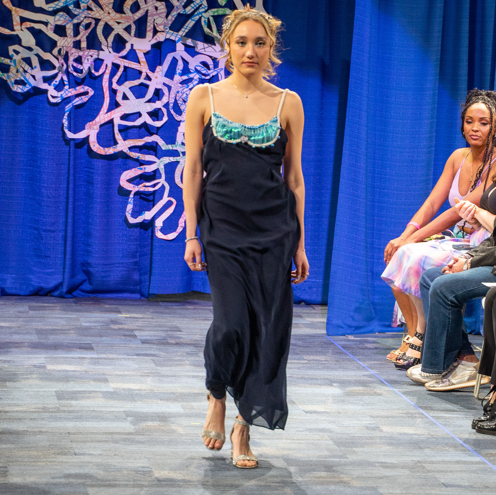 Student model in black dress walking down runway